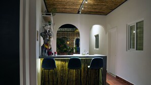 Una cucina con angolo bar, tre sedie, una statua decorativa e vista attraverso un arco.
