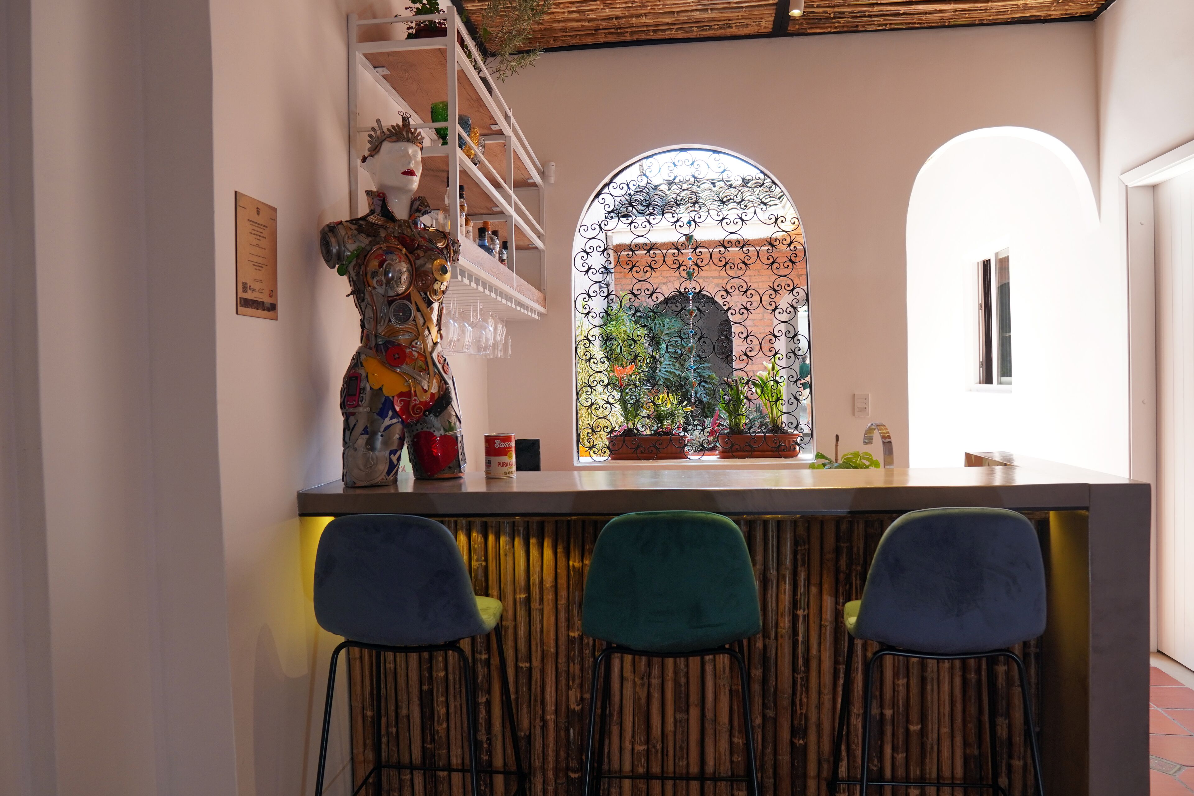 Un coin bar avec trois chaises, une sculpture décorative et une fenêtre offrant une vue en arc de cercle sur un jardin.