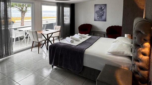 A modern hotel room with a large bed, a dining area with a table and chairs, and a view of the sea. - İdeal Butik Otel (Arnavutköy)