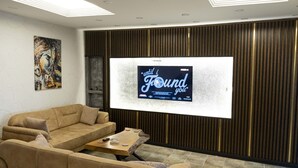 A modern living room with a large flat-screen TV mounted on a wooden wall, a beige sofa, and a small coffee table. - İdeal Butik Otel (Arnavutköy)