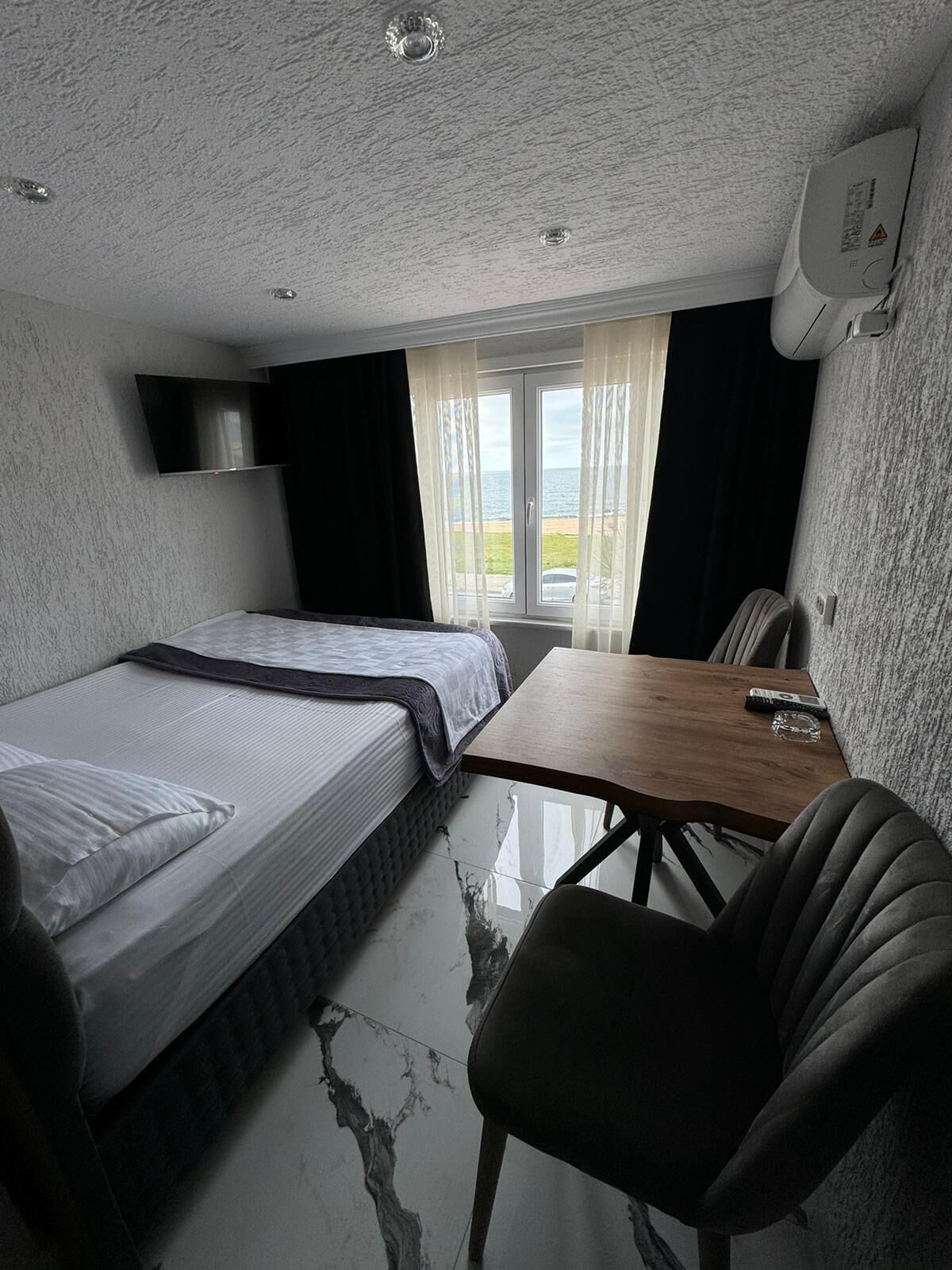 A compact hotel room with a bed, a small table, a chair, and a window with curtains.