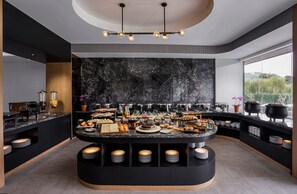 A modern breakfast buffet with a marble backsplash, a variety of food items, and a central island with stacked plates. - Forest Hills Hotel Ciwidey (Pasirjambu)