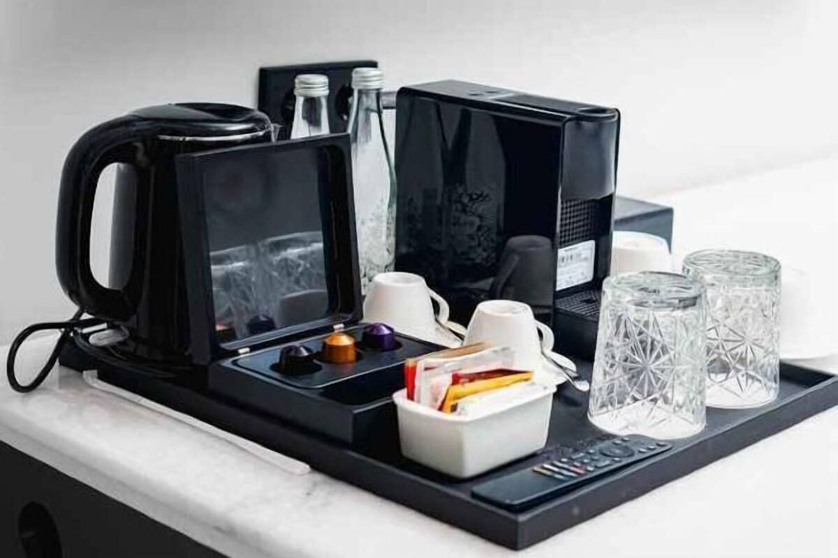 Een koffiehoek met een koffiezetapparaat, bekers, glazen en een afstandsbediening op een dienblad.