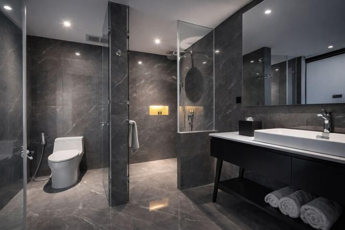 A modern bathroom with a glass-enclosed shower, a white toilet, a large mirror, and a dark vanity with towels.