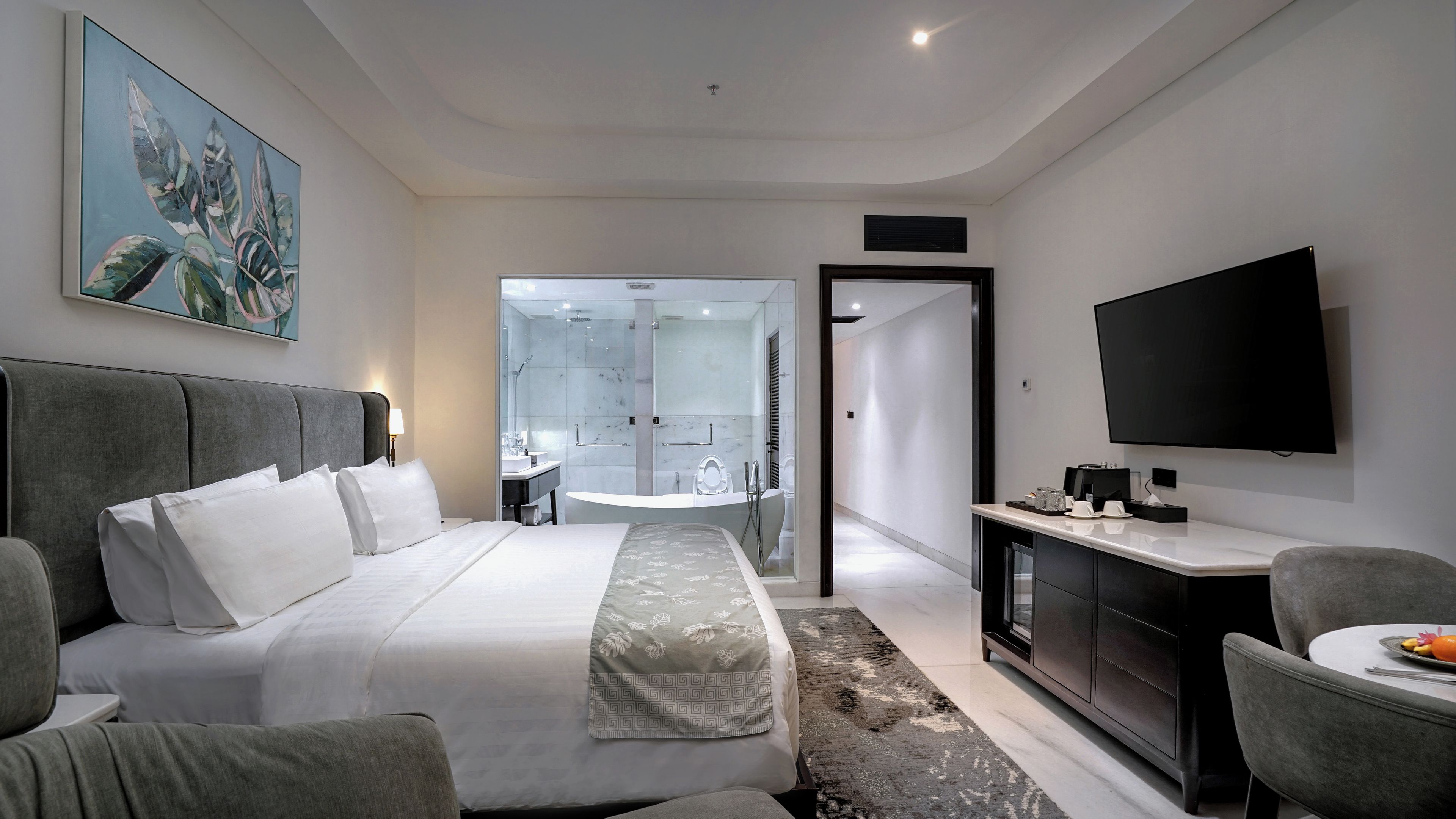 Habitación de hotel moderna con una cama grande, un escritorio, un televisor de pantalla plana y un baño con ducha de vidrio.