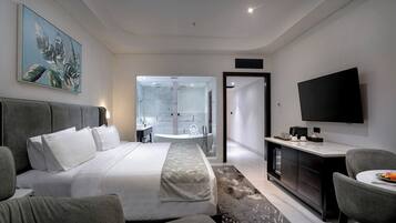 Habitación de hotel moderna con una cama grande, un escritorio, un televisor de pantalla plana y un baño con ducha de vidrio.