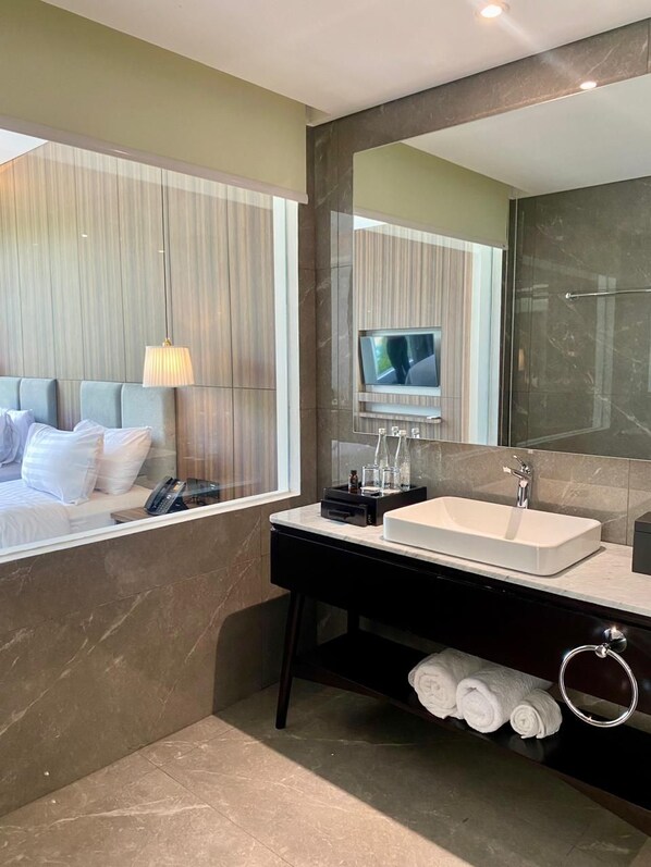 A modern bathroom with a large mirror, a sink, and a television above it. - Forest Hills Hotel Ciwidey (Pasirjambu)