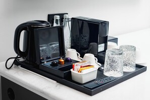 A coffee station with a coffee maker, cups, and a tray with glasses and utensils. - Forest Hills Hotel Ciwidey (Pasirjambu)