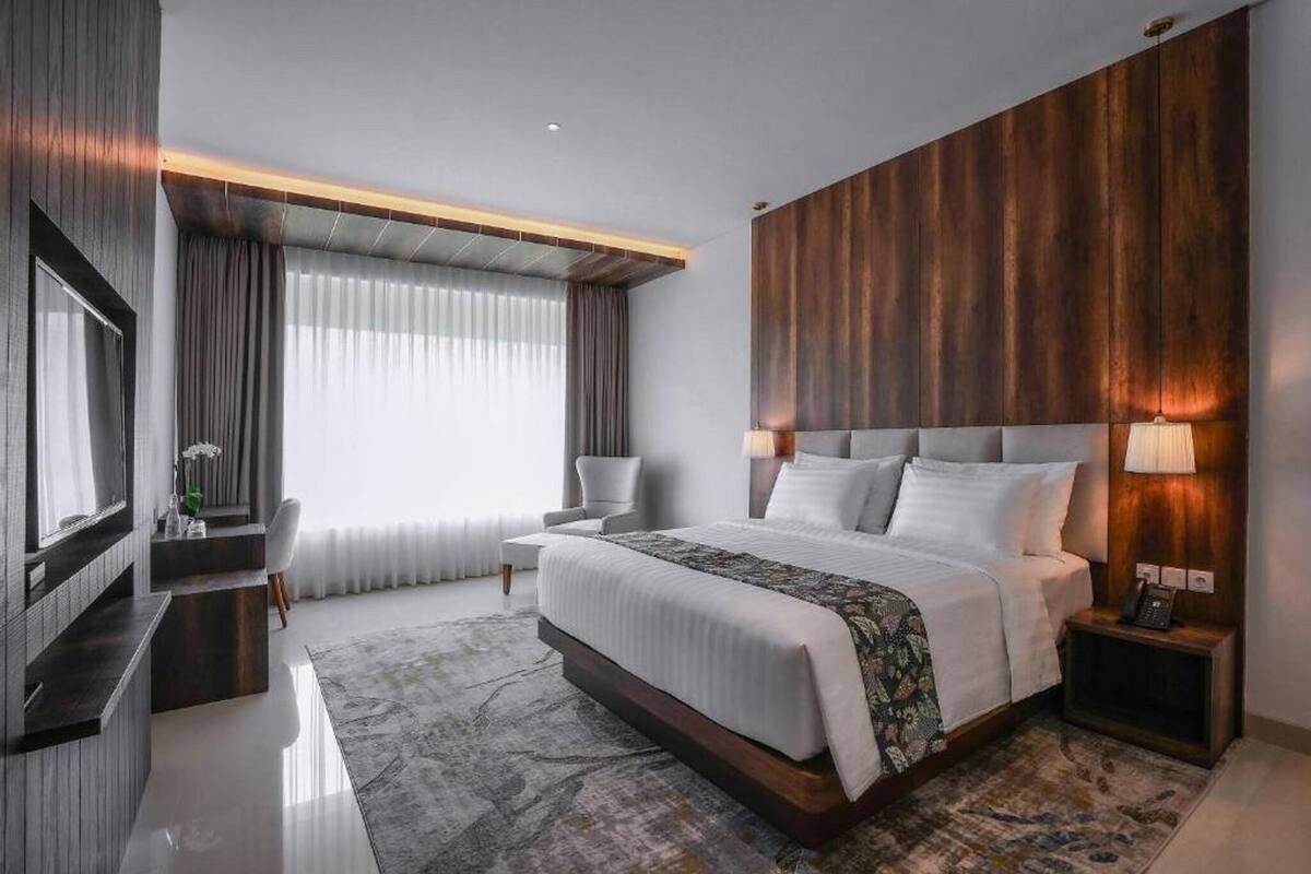 Een moderne hotelkamer met een groot bed, een televisie, een bureau en een groot raam met gordijnen.