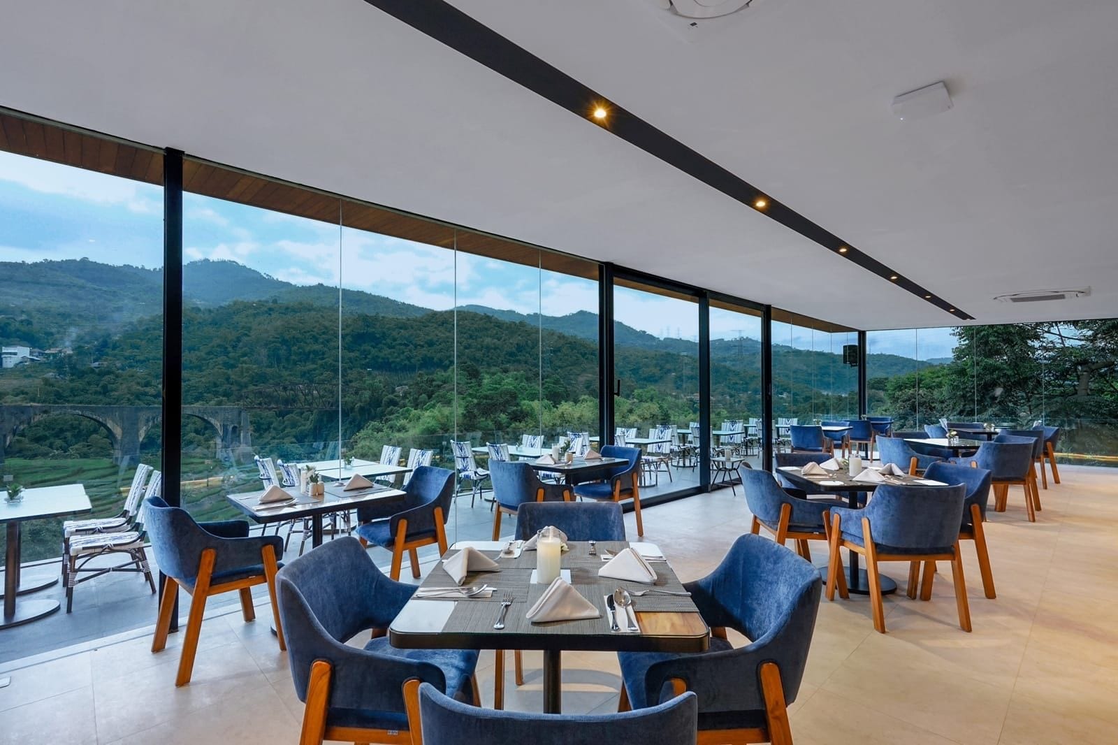 A restaurant with tables and chairs arranged in a spacious area with large windows offering a view of a mountainous landscape.