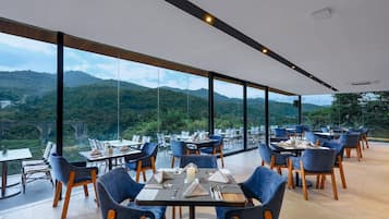A restaurant with tables and chairs arranged in a spacious area with large windows offering a view of a mountainous landscape.