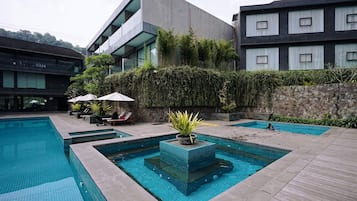 A modern hotel with a swimming pool, outdoor seating, and a stone wall.