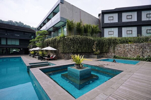 A modern hotel with a swimming pool, outdoor seating, and a stone wall. - Forest Hills Hotel Ciwidey (Pasirjambu)