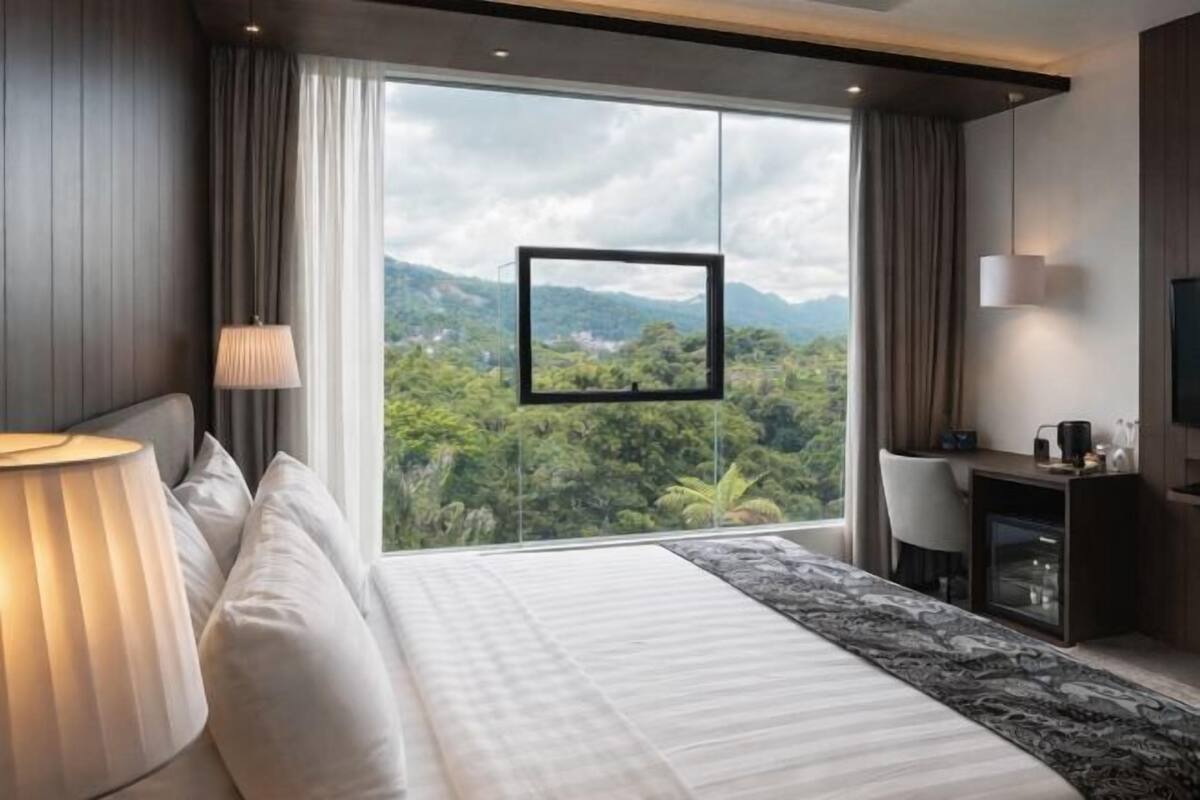 Een moderne hotelkamer met een groot bed, een bureau, een stoel, een televisie en uitzicht op een bergachtig landschap.