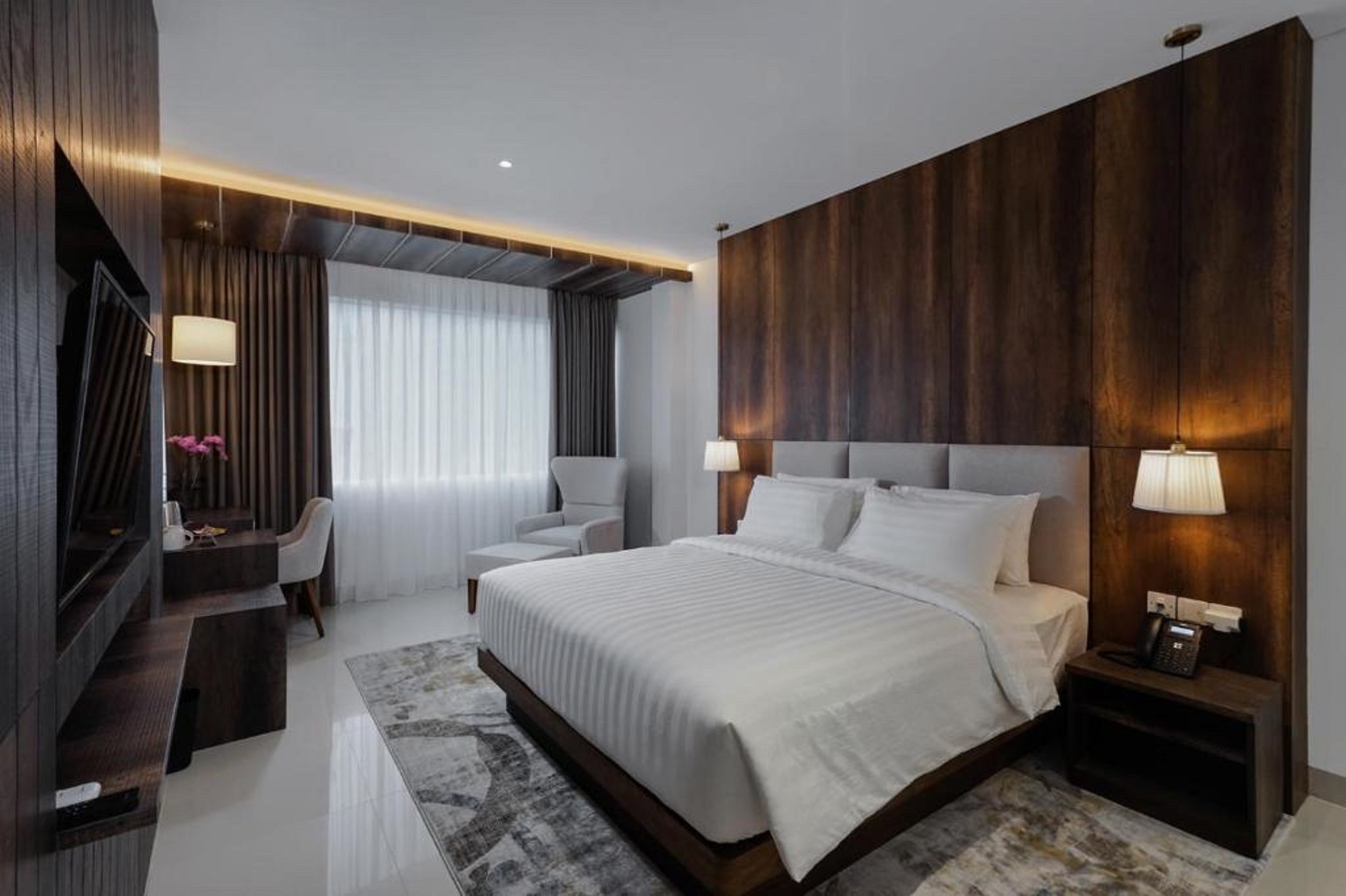A modern hotel room with a large bed, a desk, a chair, and a TV.