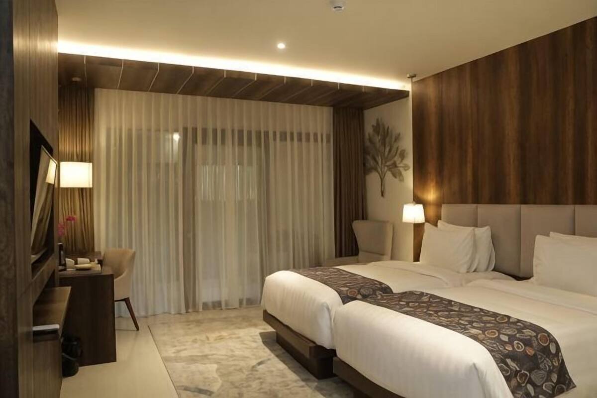 Een hotelkamer met twee bedden, een bureau, een stoel en een groot raam met gordijnen.