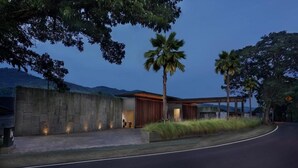 Un edificio moderno con fachada de concreto, un espacio exterior cubierto y una palmera.