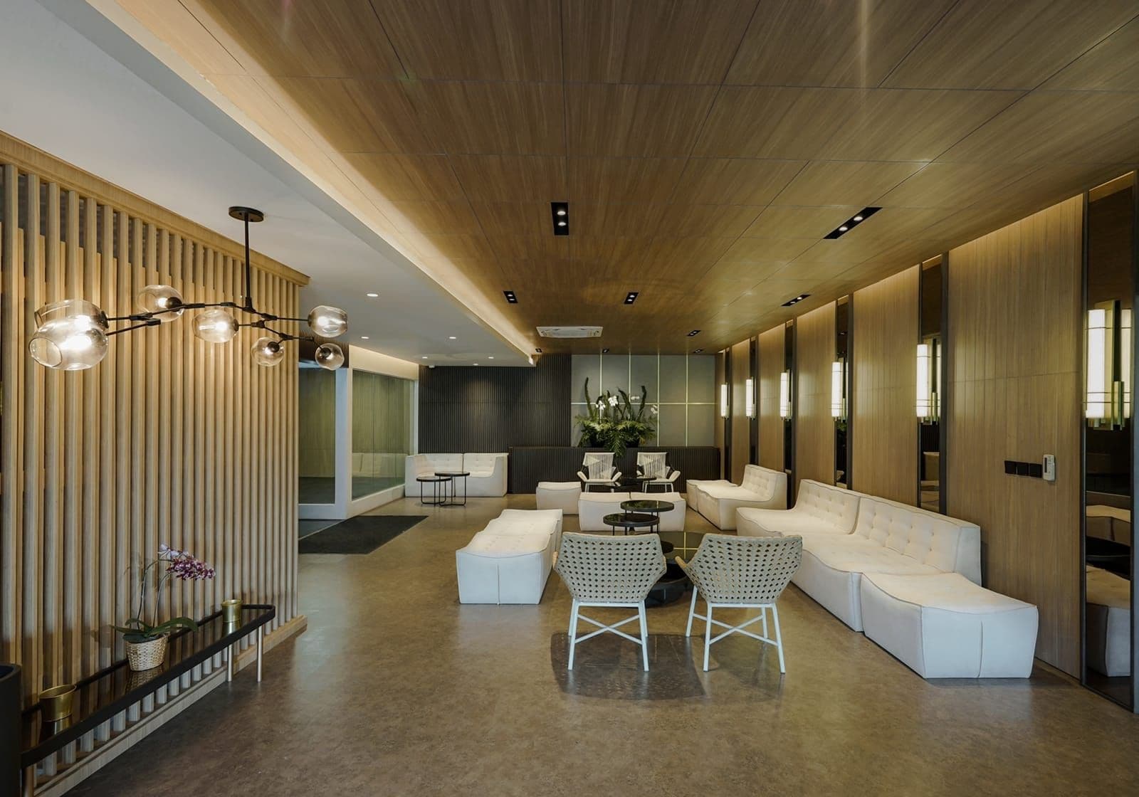 Een modern interieur met een lange receptiebalie, witte banken, een bijzettafeltje en een houten plafond.