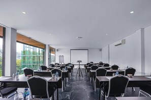 A conference room with tables, chairs, a projector screen, and a large window offering a view of greenery. - Forest Hills Hotel Ciwidey (Pasirjambu)