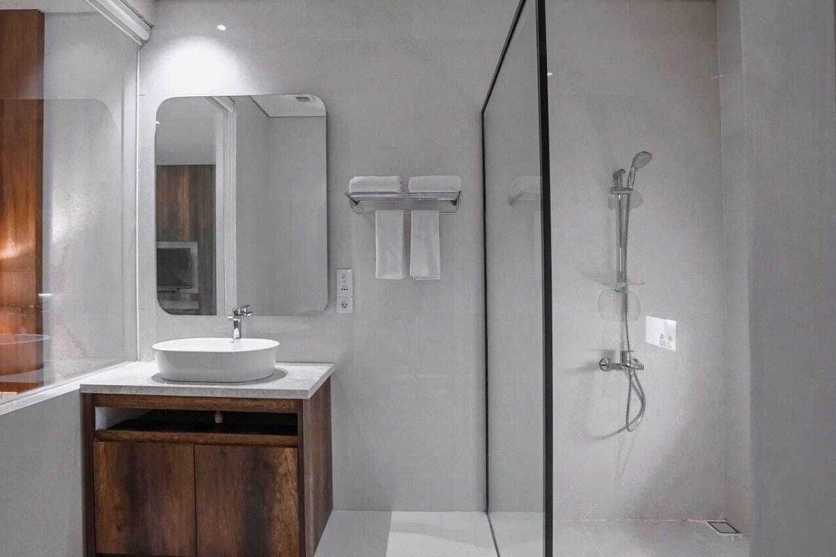 A modern bathroom with a round sink, a mirror, a shower, and a wooden cabinet.