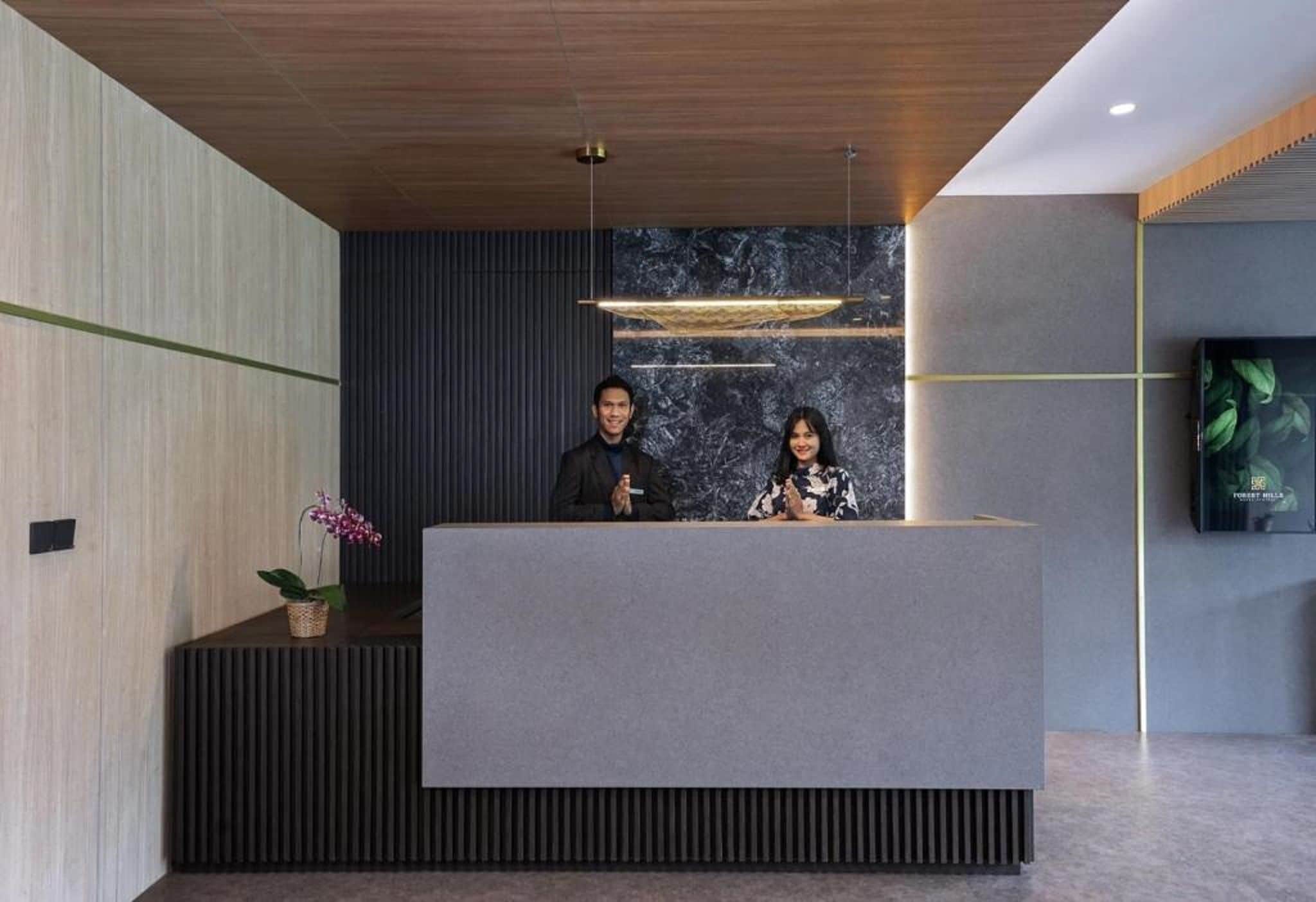 A reception desk with two staff members, a marble wall, and a television screen.
