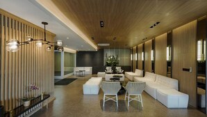 Un interior moderno con una larga recepción, sofás blancos, una mesa de centro y un techo de madera.