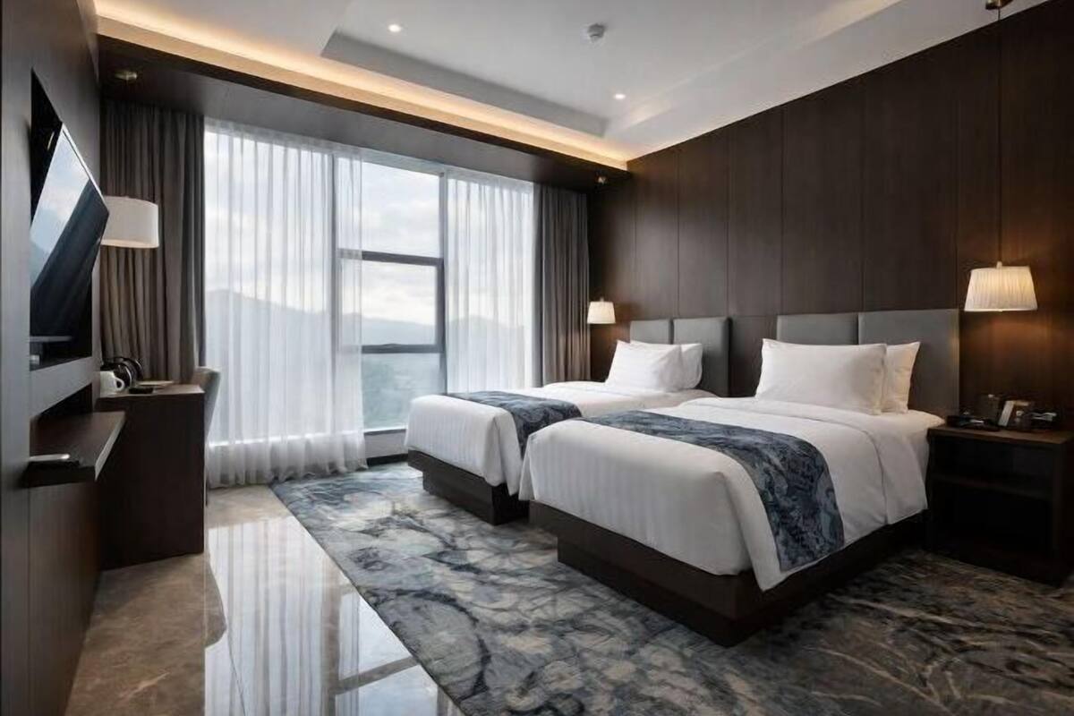 Een hotelkamer met twee bedden, een televisie, een bureau en een groot raam met gordijnen.