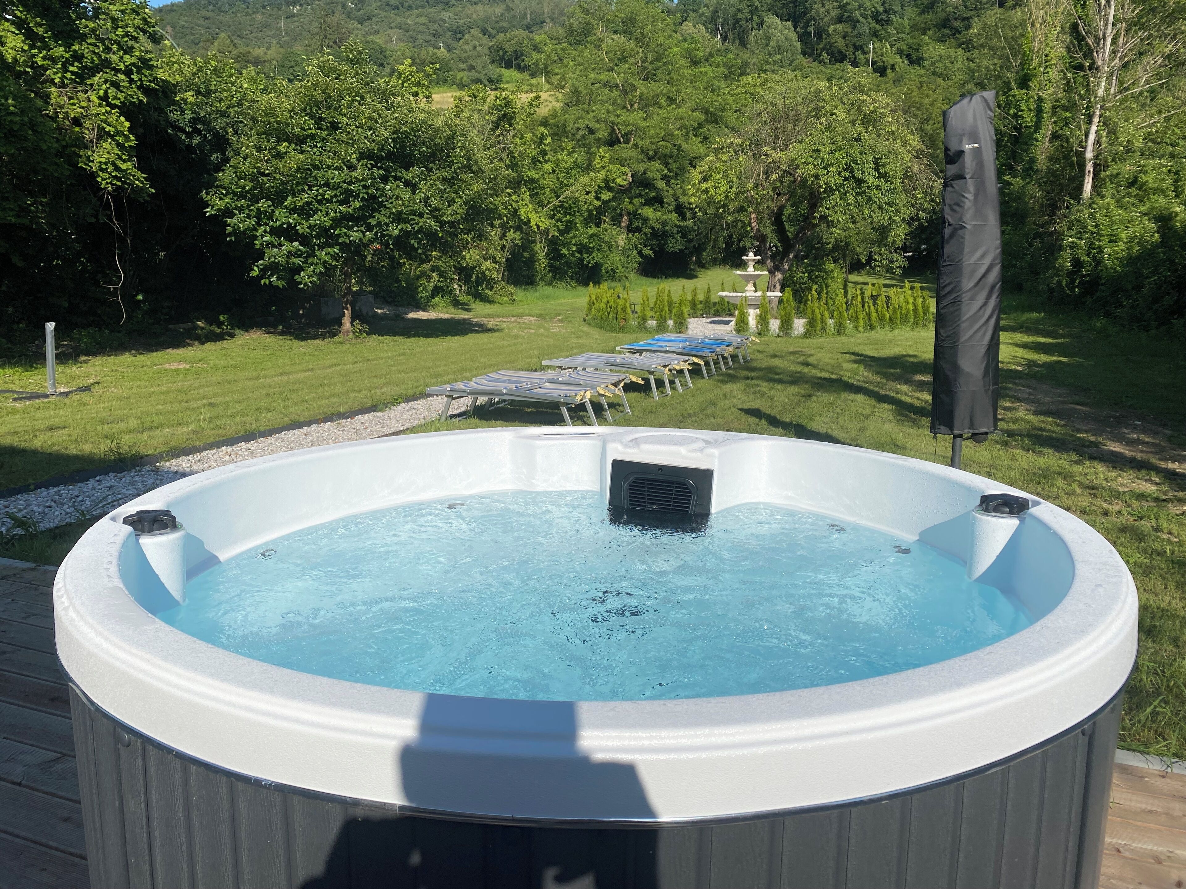 A hot tub surrounded by a wooden deck, with a grassy area and trees in the background.