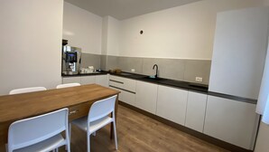 Una cocina compacta con una mesa de madera y sillas blancas, un grifo negro y una cafetera.
