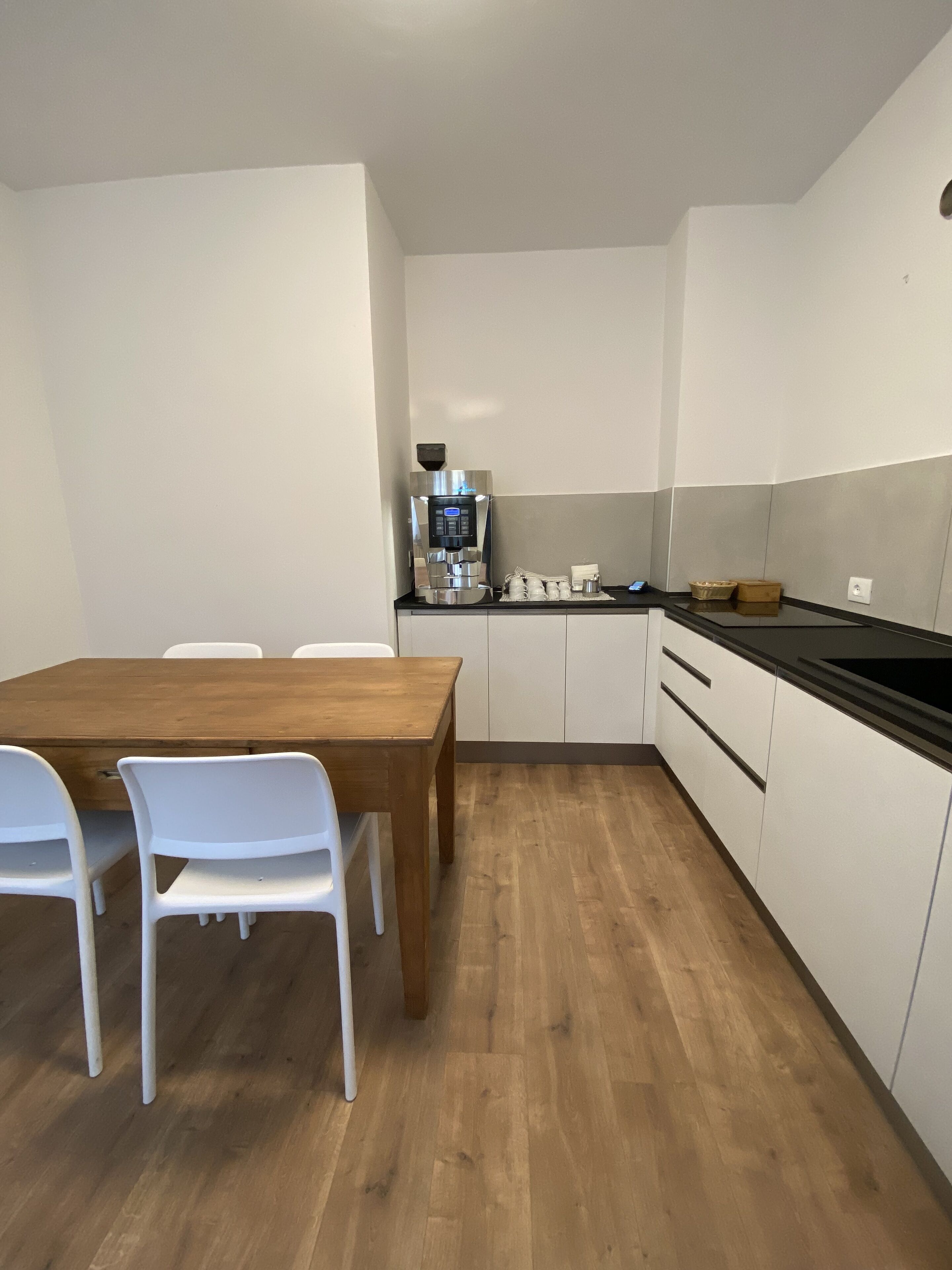 A modern kitchen with white cabinets, a wooden dining table, and white chairs.