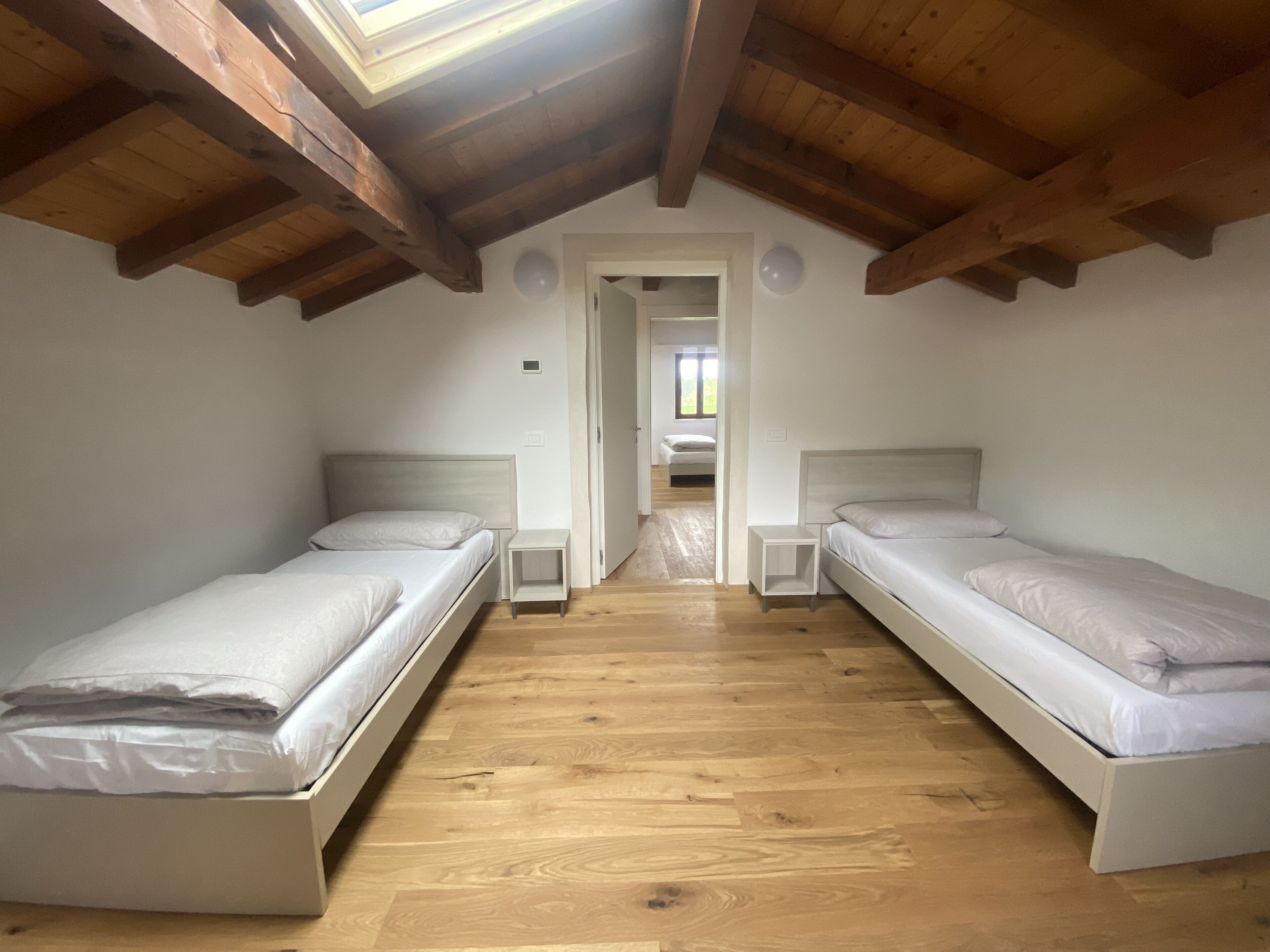 A bedroom with two single beds, wooden flooring, and a sloped ceiling with exposed beams.