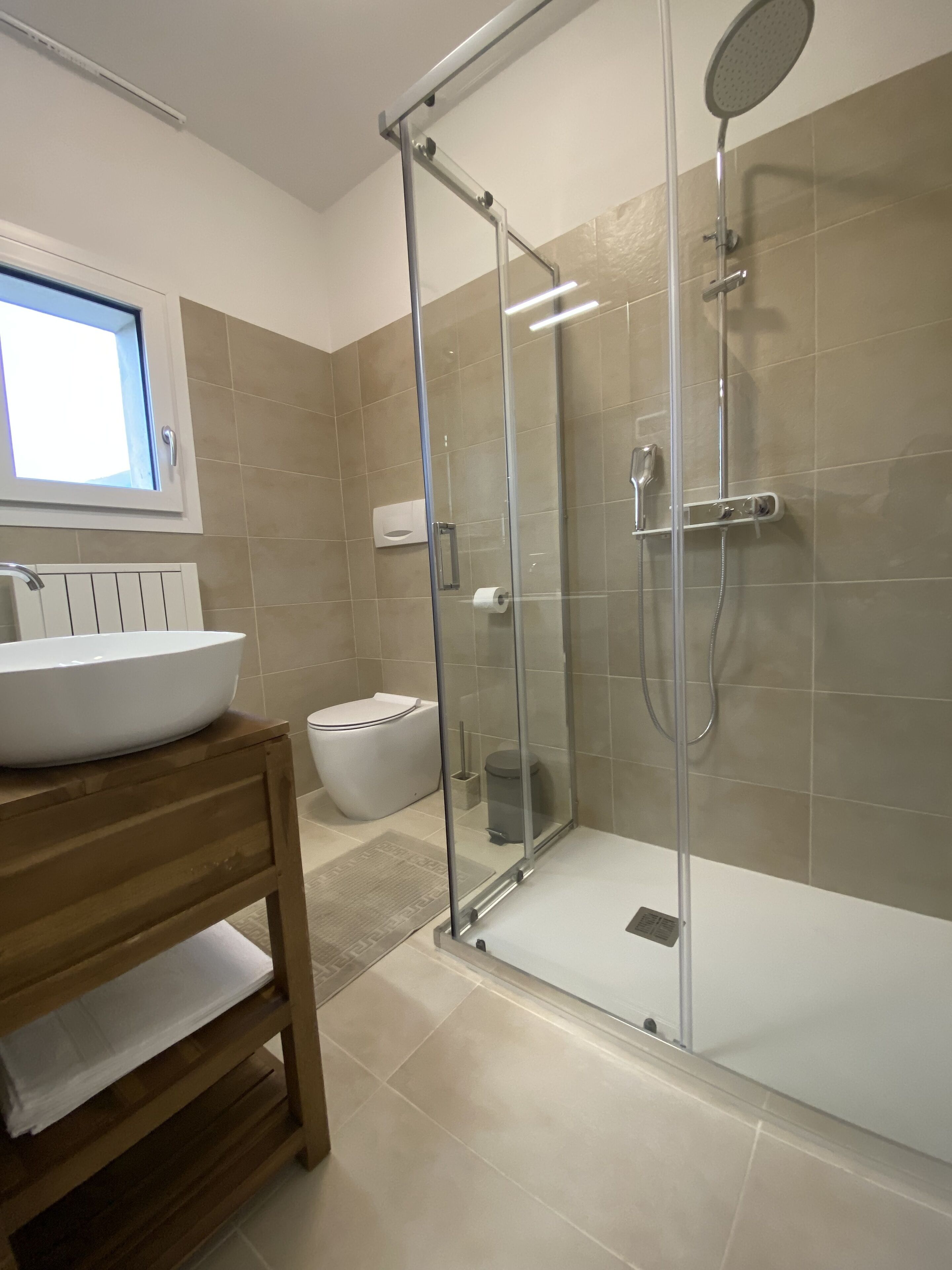 Un baño moderno con ducha acristalada, lavamanos blanco y tocador de madera.