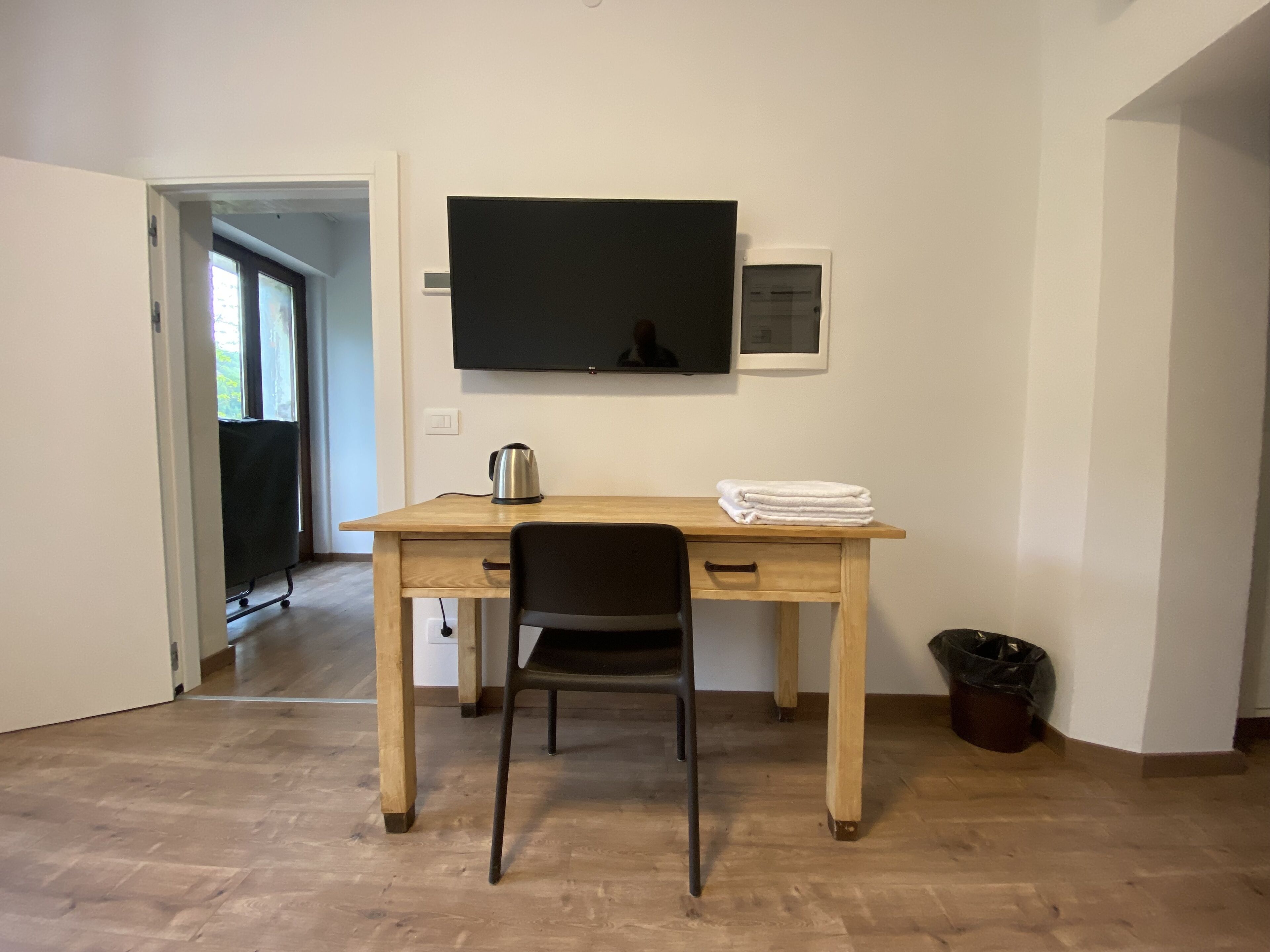 A small, tidy room with a wooden desk, a chair, a television mounted on the wall, and a window with curtains.