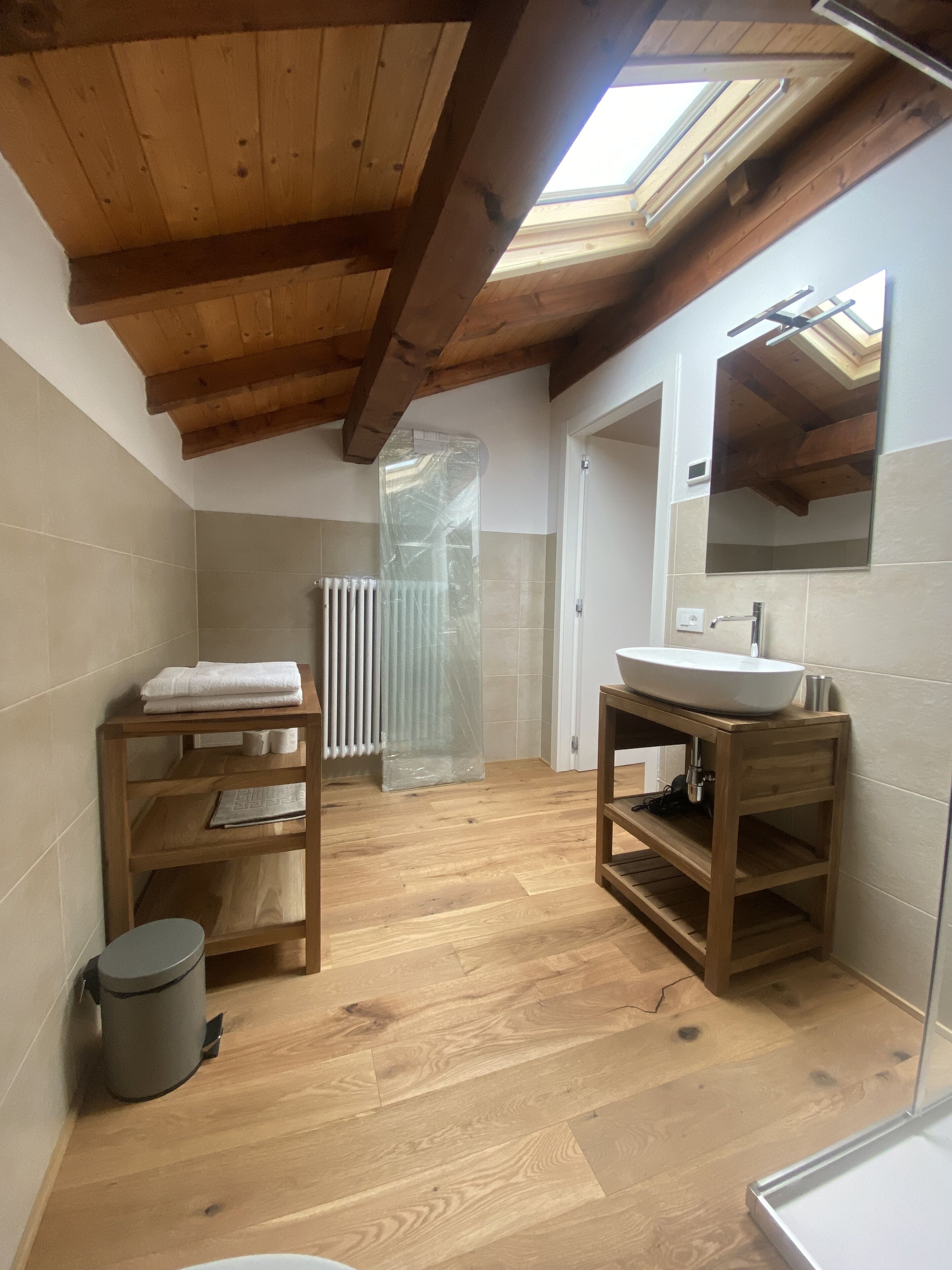 A bathroom with wooden beams, a skylight, a sink, a mirror, and a shower area.