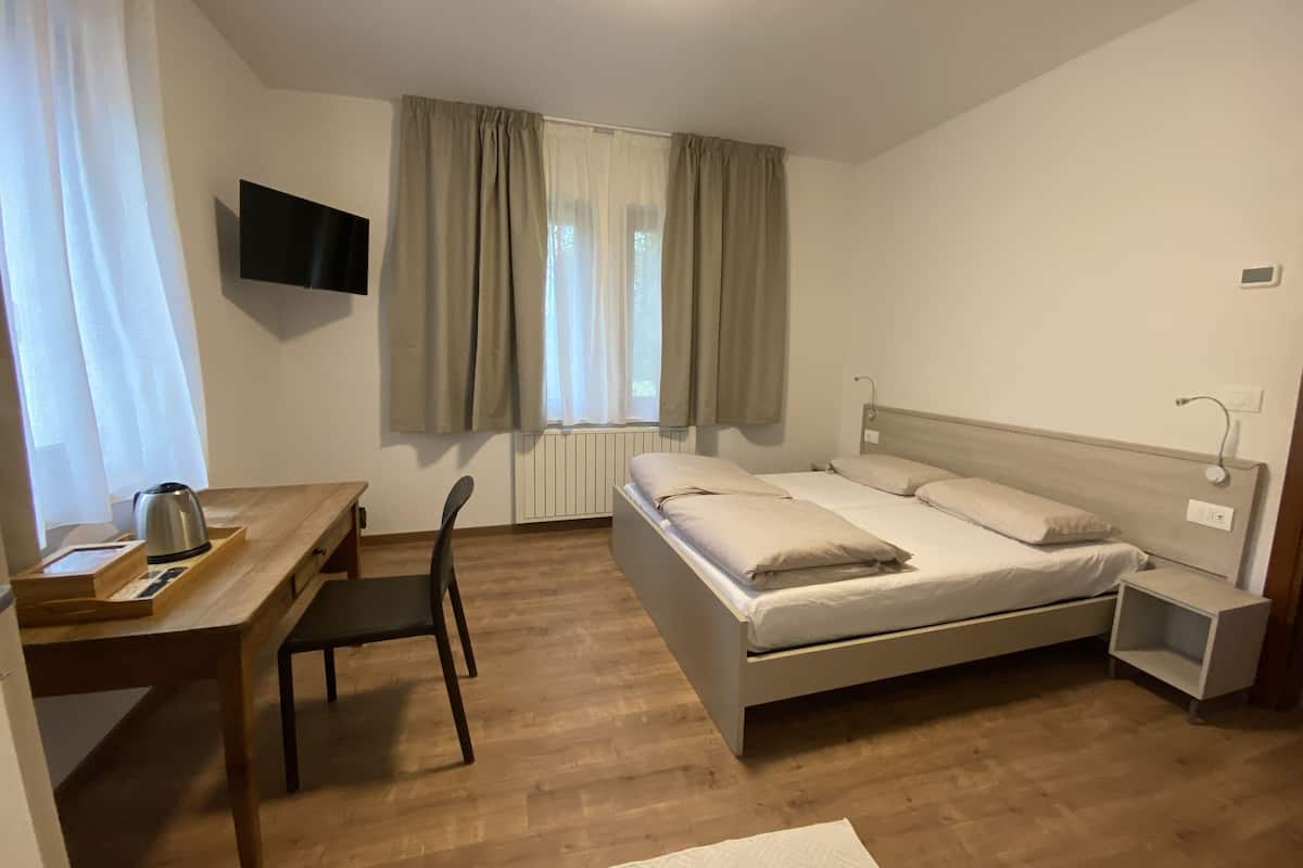 Hotellihuone, jossa on sänky, työpöytä, tuoli, televisio ja ikkuna, jossa on verhot.
