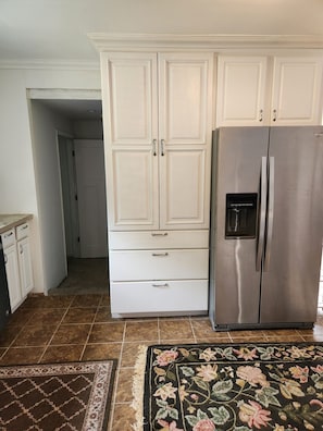 A kitchen with white cabinets, a stainless steel refrigerator, and a patterned rug.