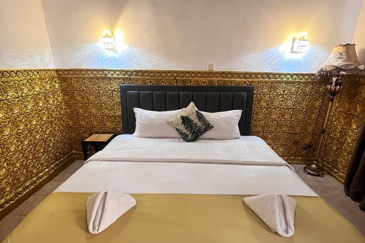 Een netjes opgemaakt bed met een zwart hoofdeinde, twee kussens en een opgevouwen handdoek.