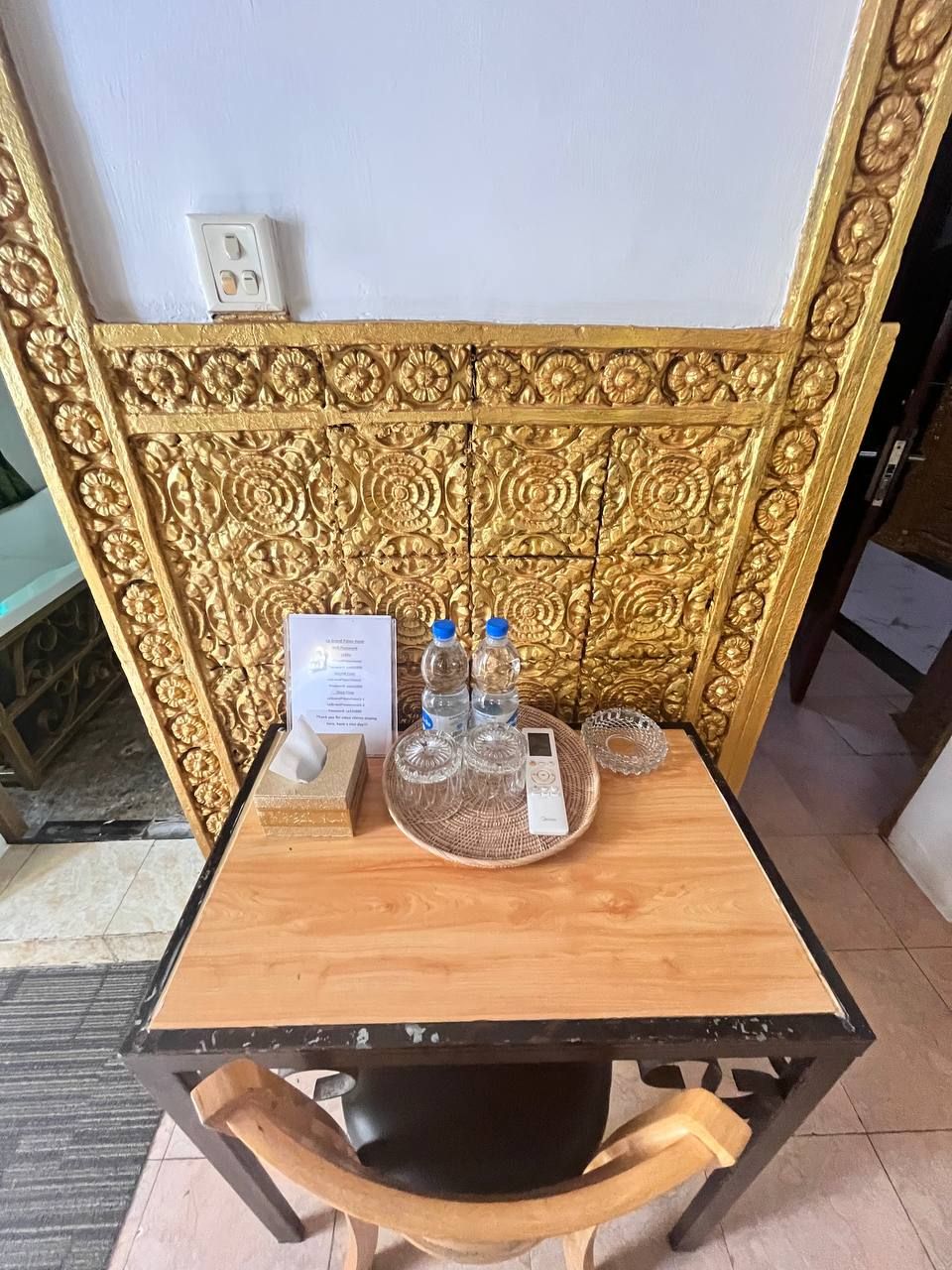 A wooden table with a black metal frame, a decorative golden headboard, and a small white device on the table.