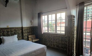 Een slaapkamer met een bed, een stoel, een raam met gordijnen en behang met patronen.