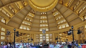Een ruime markthal met hoge plafonds en grote ramen, met tal van kraampjes en een centrale klok.