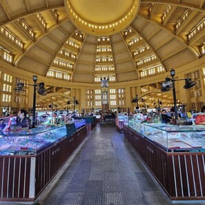 Een ruime markthal met hoge plafonds en grote ramen, met tal van kraampjes en een centrale klok.