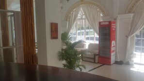 A reception area with a red vending machine, a potted plant, and a white sofa. - Le Hotel Hotel (Phnom Penh)