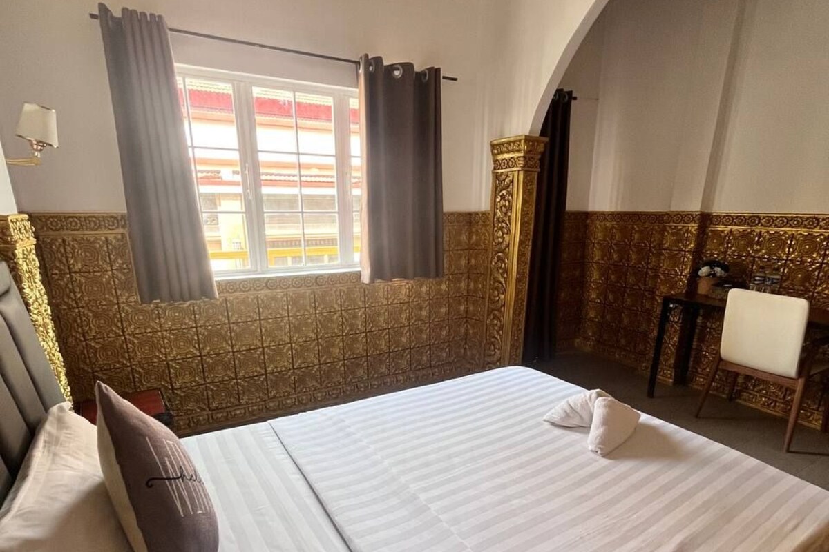 Una camera d'albergo con un letto grande, una finestra con tende, una scrivania con una sedia e piastrelle decorative alle pareti.
