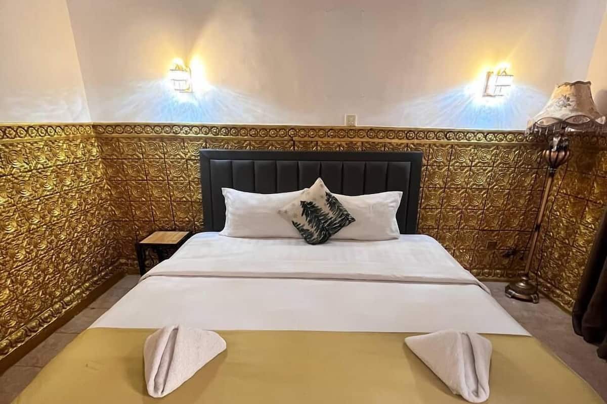Een netjes opgemaakt bed met een zwart hoofdeinde, twee kussens en een opgevouwen handdoek.