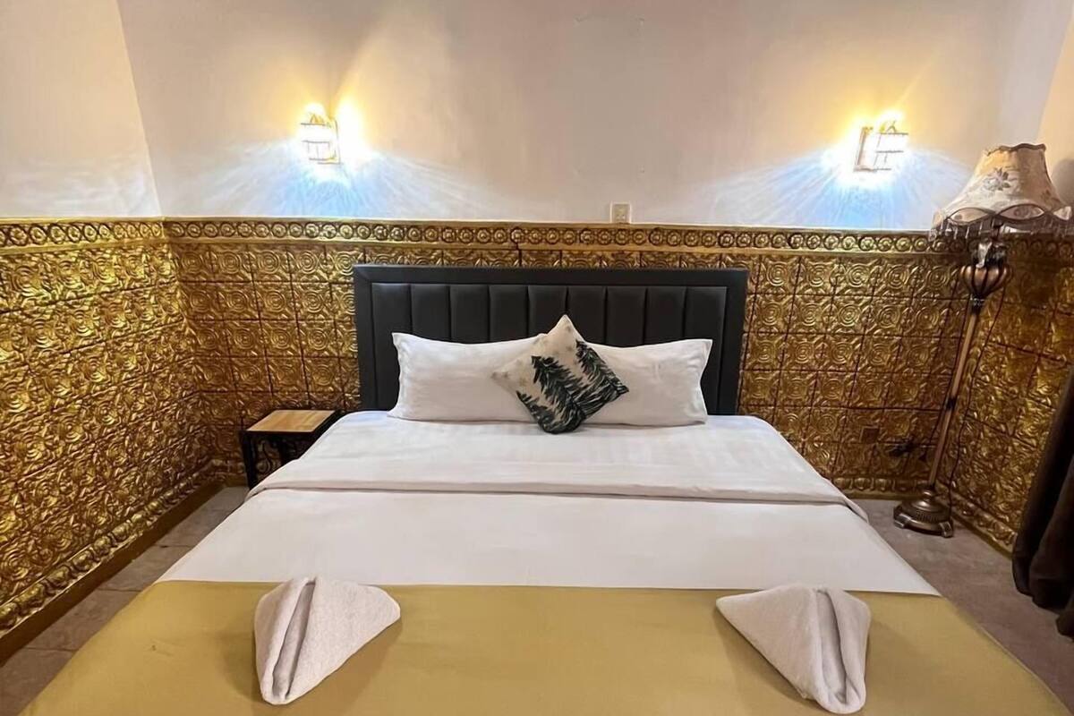 Un lit bien fait, avec une tête de lit noire, deux oreillers et une serviette pliée posée sur le lit.