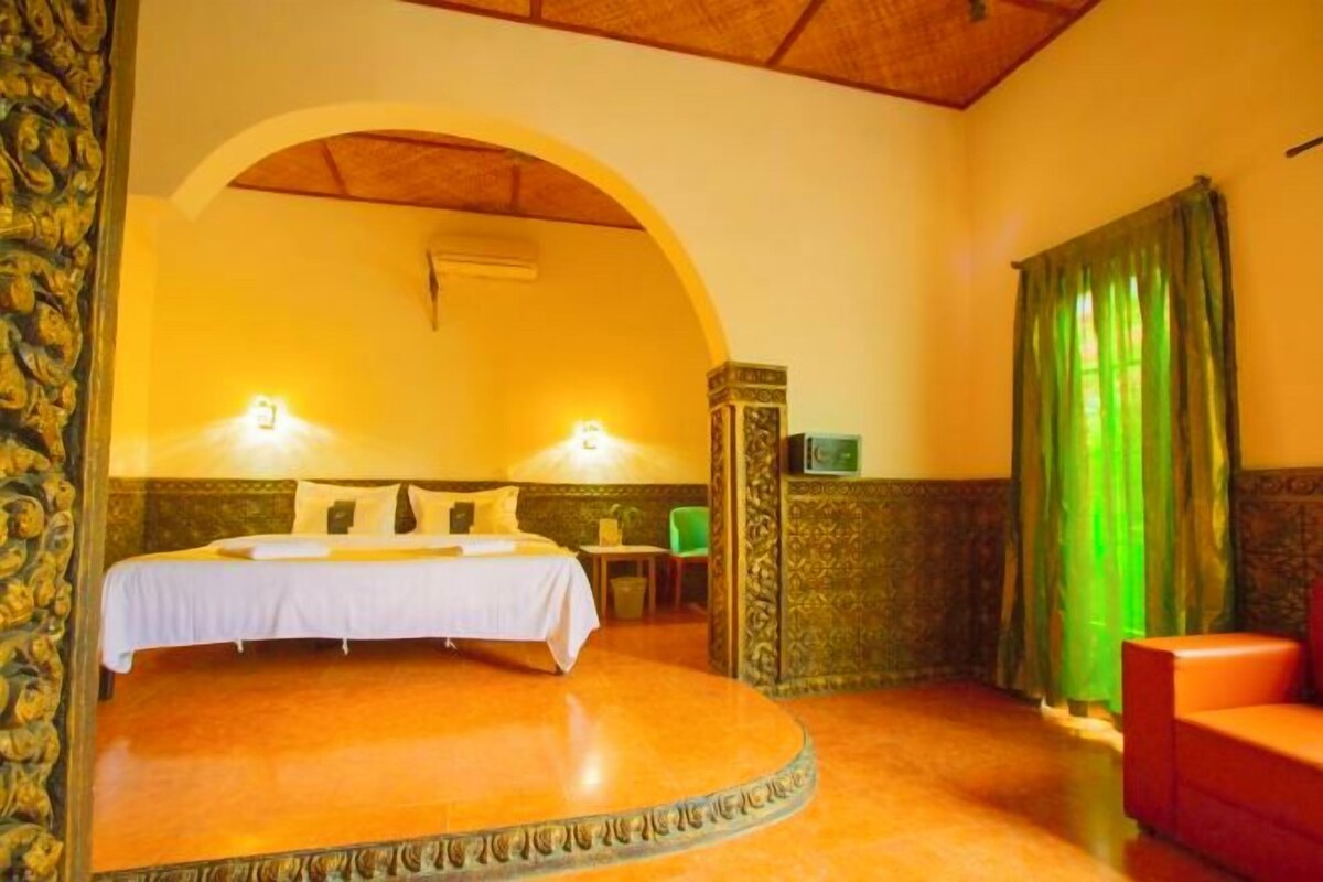 Una habitación con una cama curvada, dos lámparas de noche, una mesita pequeña y una silla roja.