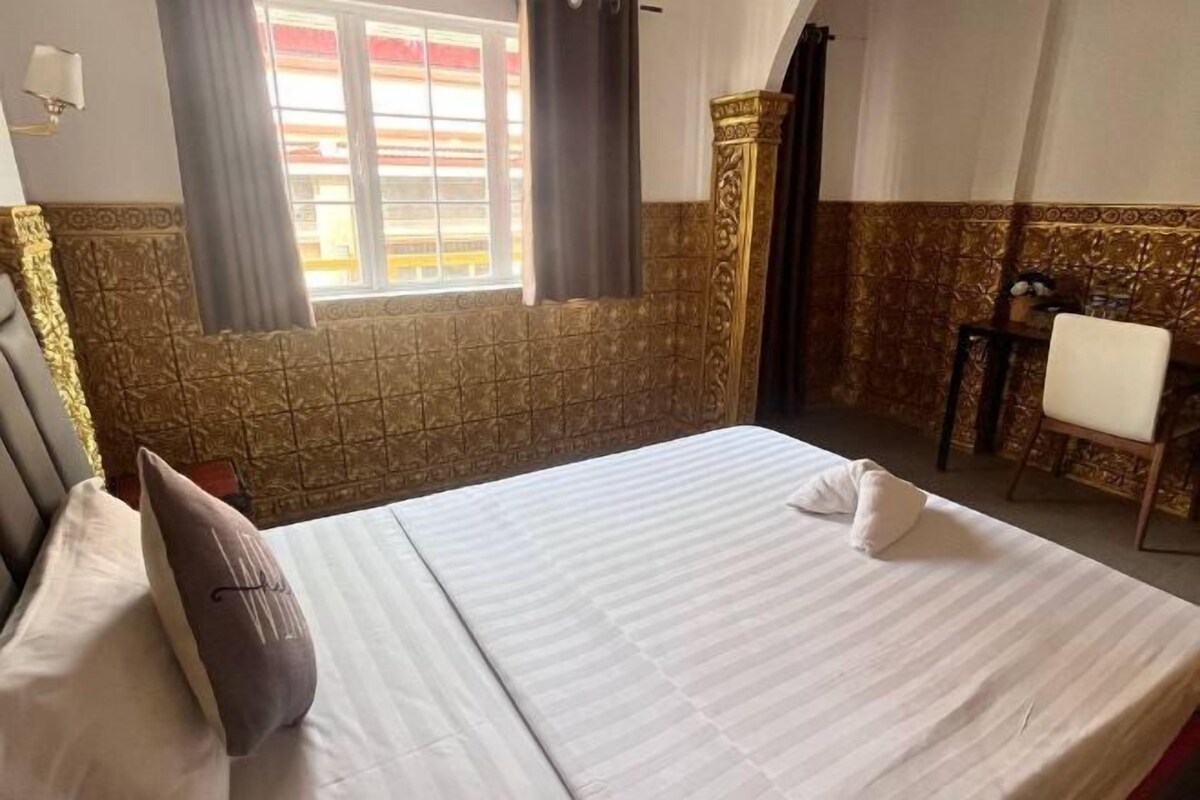 Una camera d'albergo con un letto, una sedia, una finestra con tende e una parete decorativa.