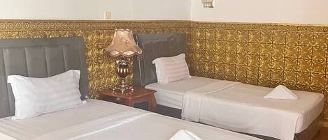 Habitación de hotel con dos camas individuales, una mesita de noche con lámpara y un panel decorativo en la pared.