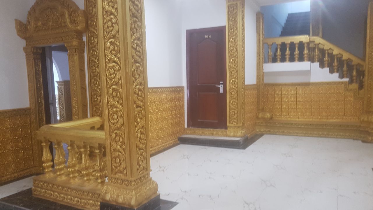 An ornate room with a golden railing, a wooden door, and a staircase with golden balustrades.