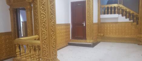 An ornate room with a golden railing, a wooden door, and a staircase with golden balustrades.